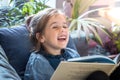 Little girl is reading a book in the living room on the couch Royalty Free Stock Photo