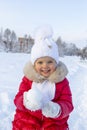 Little beautiful girl in a red coat and white scarf holds a round snowball in her hands and smiles. Snow-covered path and