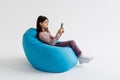 Little beautiful girl sitting on a beanbag holds mobile playing isolated on a white background Royalty Free Stock Photo