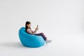 Little beautiful girl sitting on a beanbag holds mobile playing isolated on a white background Royalty Free Stock Photo