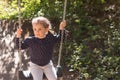 Little beautiful girl smiling swings on a swing in the park against the background of blurred foliage Royalty Free Stock Photo