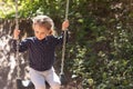 Little beautiful girl smiling swings on a swing in the park against the background of blurred foliage Royalty Free Stock Photo