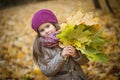 Little beautiful girl stands with a bouquet of maple orange leaves in the autumn park. She looks away and smiles. Dressed in a Royalty Free Stock Photo