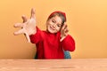 Little beautiful girl wearing casual clothes sitting on the table looking at the camera smiling with open arms for hug Royalty Free Stock Photo