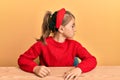 Little beautiful girl wearing casual clothes sitting on the table looking to side, relax profile pose with natural face with Royalty Free Stock Photo