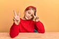 Little beautiful girl wearing casual clothes sitting on the table smiling looking to the camera showing fingers doing victory sign Royalty Free Stock Photo