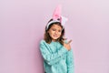 Little beautiful girl wearing cute easter bunny ears cheerful with a smile of face pointing with hand and finger up to the side Royalty Free Stock Photo