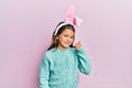 Little beautiful girl wearing cute easter bunny ears smiling with happy face looking and pointing to the side with thumb up Royalty Free Stock Photo