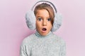 Little beautiful girl wearing fluffy earmuff afraid and shocked with surprise and amazed expression, fear and excited face Royalty Free Stock Photo