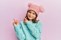 Little beautiful girl wearing wool sweater and cute winter hat smiling and looking at the camera pointing with two hands and Royalty Free Stock Photo