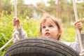 Little beautiful red-haired girl riding a black wheel tied with ropes on a hot summer day outdoors Royalty Free Stock Photo