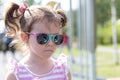 Little beautiful sad girl in sun-protective glasses with pigtails stands on the street Royalty Free Stock Photo