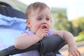 little, beautiful, smiling, cute redhead baby in a pram out-of-doors in a sleeveless shirt holding fingers in his mouth Royalty Free Stock Photo