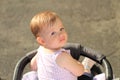 little, beautiful, smiling, cute redhead baby in a sleeveless shirt in a pram out-of-doors drops hands down and looking back Royalty Free Stock Photo