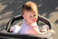 little, beautiful, smiling, cute redhead baby in a sleeveless shirt in a pram out-of-doors drops hands down and looking back Royalty Free Stock Photo