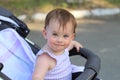 little, beautiful, smiling, cute redhead baby in a sleeveless shirt in a pram out-of-doors drops hands down and looking forward Royalty Free Stock Photo