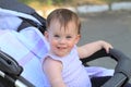 little, beautiful, smiling, cute redhead baby in a sleeveless shirt in a pram out-of-doors drops hands down and looking forward Royalty Free Stock Photo