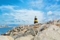 Little beautiful white, yellow and black lighthouse standing over the big stones at the pier of Benalmadena port, panoramic view Royalty Free Stock Photo