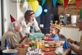 Little birthday girl recieving a present from her grandmother, family together at kitchen table celebrating birthday of little