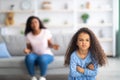 Little black girl feeling angry, taking offence at her mother at home, copy space. Parent child conflict concept