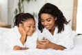 Little black girl and her mom listening music on smartphone, wearing bathrobes Royalty Free Stock Photo