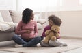 Little black girl sitting on floor with pregnant mom, cuddling bear Royalty Free Stock Photo