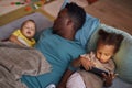 Little Black girl using smartphone with sleeping father at naptime