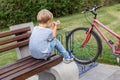 Little blond alone upset boy in casual jeans wear sitting on wooden bench in park. Lonely unhappy kid outdoors Royalty Free Stock Photo