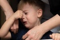 A little blond boy, age 3, is crying and his mother calms him down. female hands close-up on a black background