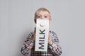 Little blond boy is holding a big white carton milk package. Light background Royalty Free Stock Photo