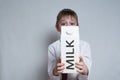 Little blond boy holds and shows a big white carton milk package. White shirt and red tie. Light background Royalty Free Stock Photo