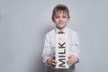 Little blond boy holds and shows a big white carton milk package. White shirt and red tie. Light background Royalty Free Stock Photo