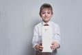 Little blond boy holds and shows a big white carton package. White shirt and red tie. Light background Royalty Free Stock Photo