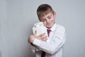 Little blond boy hugs a big white carton package. White shirt and red tie. Light background Royalty Free Stock Photo