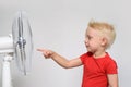 Little blond boy in a red t-shirt touches the fan with his finger. Summer concept