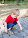 Little blond boy sitting on his haunches and picks his rod moss growing among the tiles