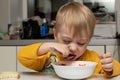 Little blond boy 3 years old is eating soup and bread in the kitchen at the table and close-up Royalty Free Stock Photo