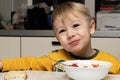 Little blond boy 3 years old is eating soup in the kitchen at the table and smiling contented close-up Royalty Free Stock Photo