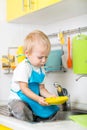 Little blond kid boy washing dishes in domestic kitchen. Happy child having fun. Royalty Free Stock Photo