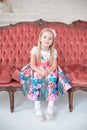 A little blond girl in colorful dress sitting on big sofa Royalty Free Stock Photo