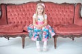 A little blond girl in colorful dress sitting on big sofa