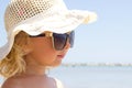 Little blond girl in glasses and hat smiling with the sea on background,positive portrait of european toddler,adorable Royalty Free Stock Photo