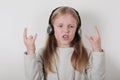 Blond girl with headphones listening music and singing. Cute little girl making a rock-n-roll sign.