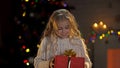 Little blond girl holding present under Christmas tree, magic winter atmosphere Royalty Free Stock Photo