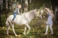 Little blond girl leading pony by bridle with her younger brother