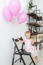 Little girl with lollipop in beautiful dress sitting on chair with pink balloons Royalty Free Stock Photo