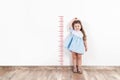 Little blond girl measuring height on white wall.