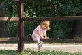 Little blond girl in pink dress climbing over the wooden fence in summer day on the forest background. Vocation in the village. Royalty Free Stock Photo