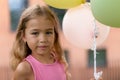 Little blond girl posing with baloons in city and looking at camera. Royalty Free Stock Photo