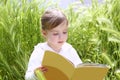 Little blond girl reading book green spikes garden Royalty Free Stock Photo